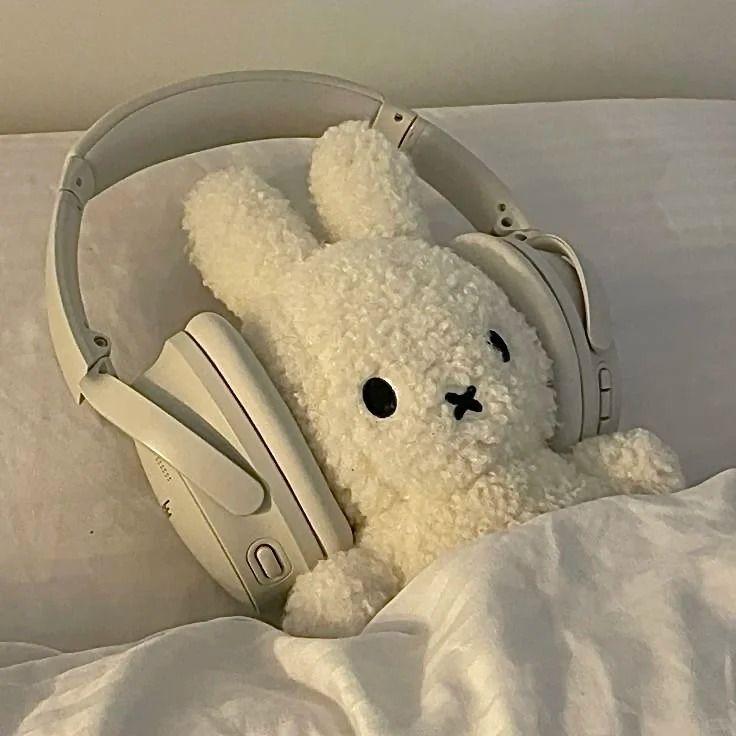 Miffy plush with headphones laying on a pillow under a white blanket